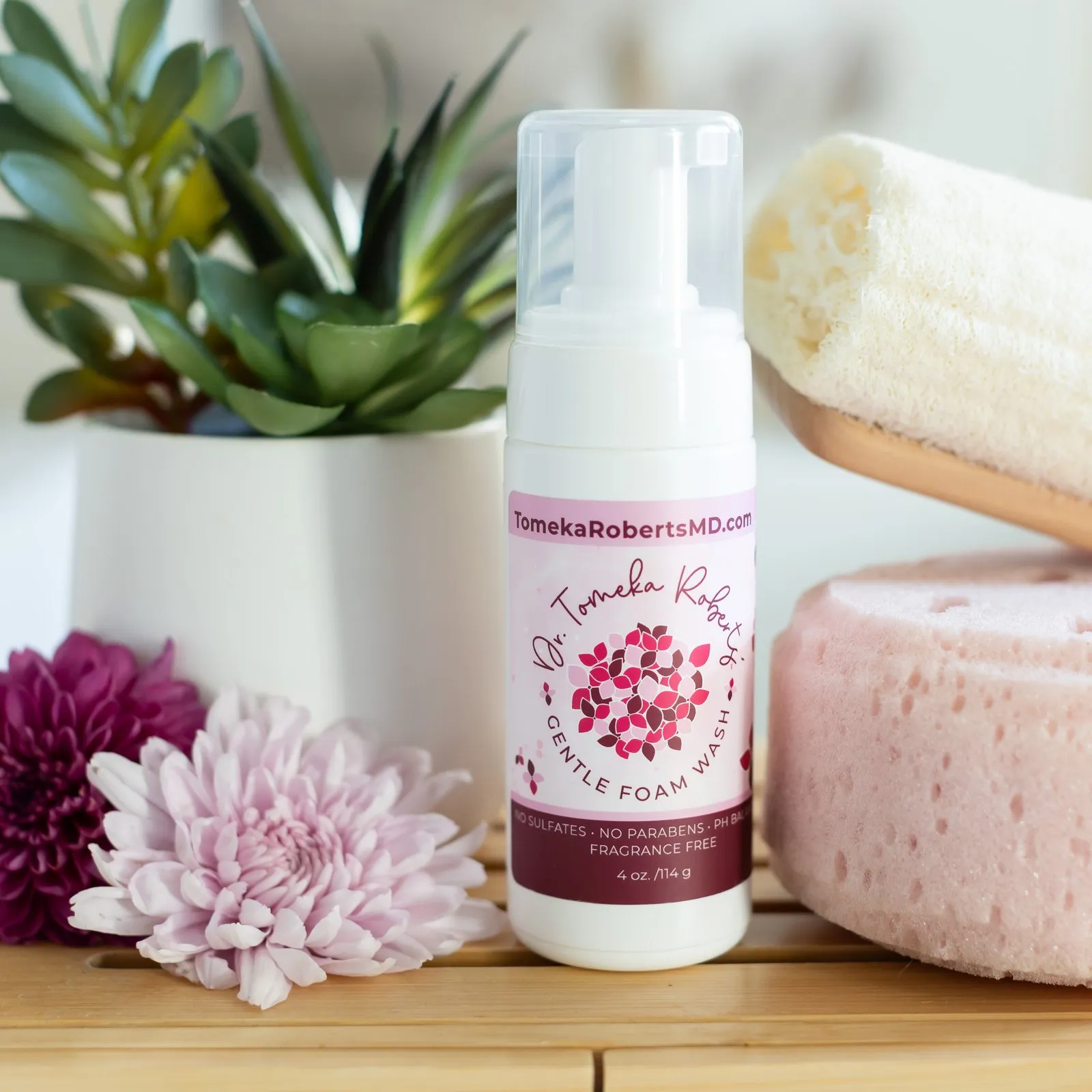 Fragrance-Free Gentle Foam Wash on a wooden tray with a loofah, bath sponge and chrysanthemums