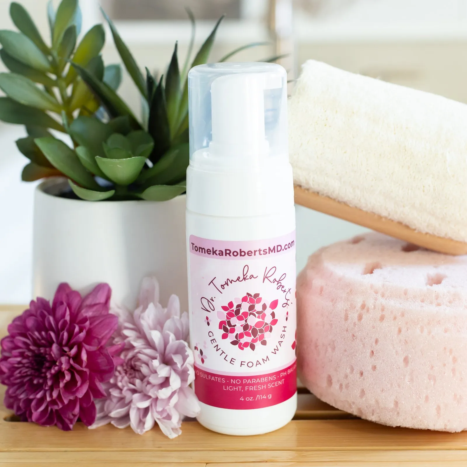 Fresh Scent Gentle Foam Wash on a wooden tray with a loofah, bath sponge and chrysanthemums